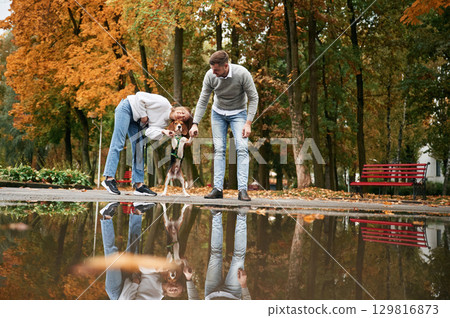 By the puddle. Lovely couple are with their cute dog outdoors 129816873