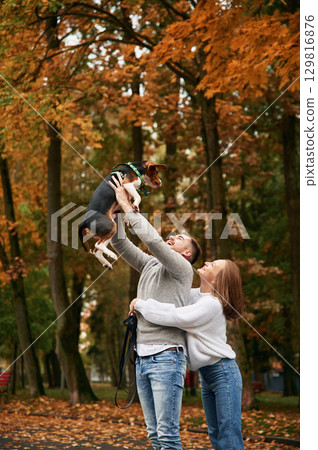 Animal is high up in man hands. Lovely couple are with their cute dog outdoors 129816876