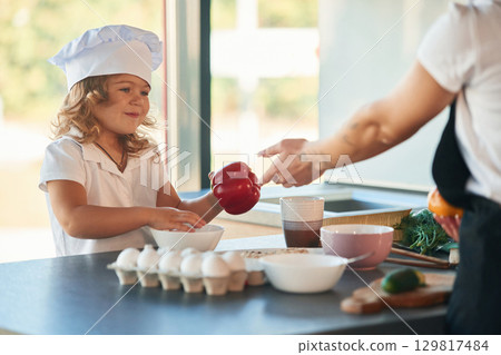 Eggs and pepper. Mother with her daughter are preparing food on the kitchen 129817484