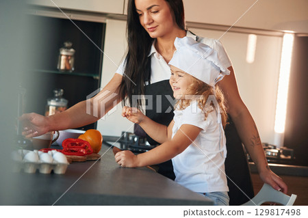 Side view. Mother with her daughter are preparing food on the kitchen Side view. Mother with her daughter are preparing food on the kitchen 129817498