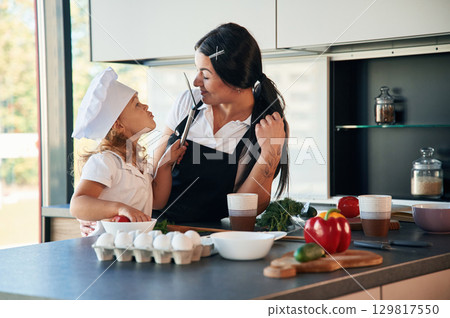 Cozy atmosphere. Mother with her daughter are preparing food on the kitchen Cozy atmosphere. Mother with her daughter are preparing food on the kitchen 129817550