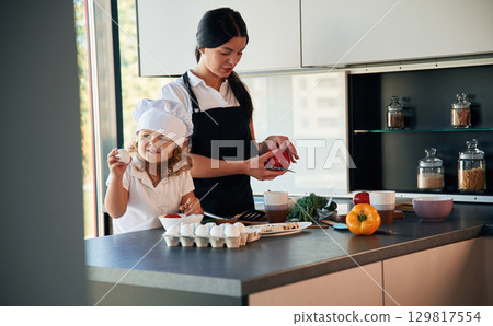 Cozy atmosphere. Mother with her daughter are preparing food on the kitchen 129817554