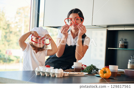 Playing with slices of pepper. Mother with her daughter are preparing food on the kitchen 129817561