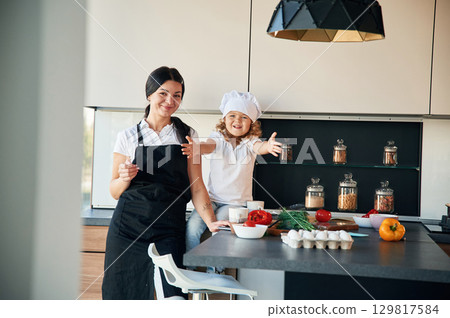 Front view. Mother with her daughter are preparing food on the kitchen 129817584