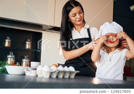 Front view. Mother with her daughter are preparing food on the kitchen Front view. Mother with her daughter are preparing food on the kitchen 129817605
