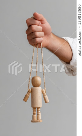 Male hand holding wooden puppet on strings against gray background. 129818680