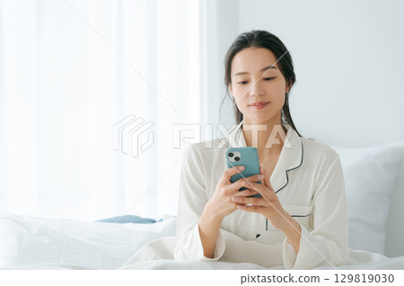 Woman operating smartphone in bed 129819030