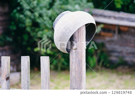 Overturned metal pot on fence post creates rustic countryside scene 129819748