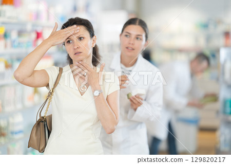 Middle-aged woman feeling pain standing with her back to female pharmacist offering remedy 129820217