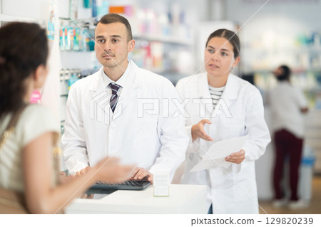 Male and female pharmacists speaking to woman customer buying medical preparation in drugstore Male and female pharmacists speaking to woman customer buying medical preparation in drugstore 129820239