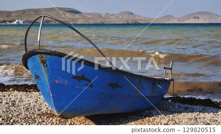 Small blue fishing boat resting on Crimean beach with dolphin and shark decorations 129820515