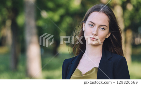 Confident businesswoman standing in park, professional attire reflecting success amid lush green landscape 129820569