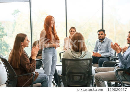 Young woman is standing and talking about herself. Group of people are having therapy meeting together 129820657
