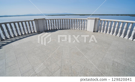 Marble terrace with ornate balusters framing serene lake waters, reflecting cloudless sky and radiating tranquil landscape atmosphere in Khabarovsk. 129820841