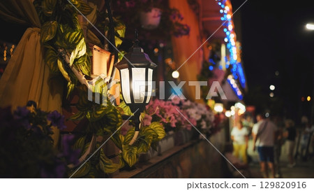 Luminous street lamp adorns a vibrant, flowered facade of a building in crimea, black sea, creating a warm and inviting atmosphere at night 129820916