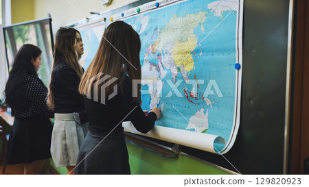 High school students engaged in a geography lesson, marking locations on a large world map 129820923