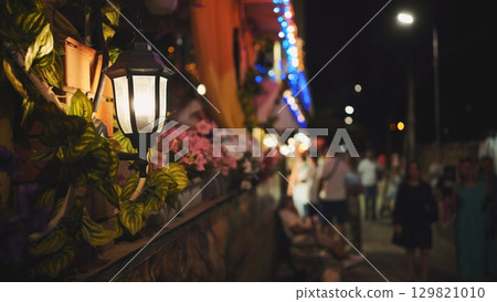 Warm street lamp casting golden glow over blurred nighttime silhouettes along black sea promenade in crimea 129821010