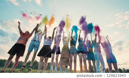 School friends joyfully leaping and tossing colorful powder in the air at sunset, commemorating their friendship and making lively memories 129821043