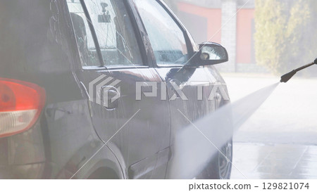 Car wash worker cleaning vehicle with high pressure water jet 129821074