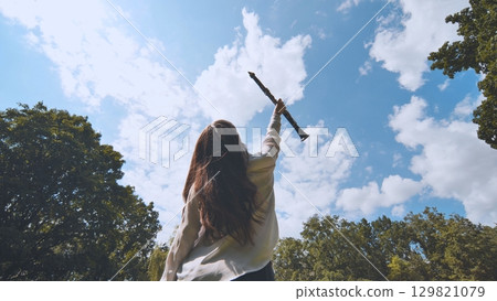 Female musician holding clarinet skyward amid verdant park landscape, expressing musical passion Female musician holding clarinet skyward amid verdant park landscape, expressing musical passion 129821079