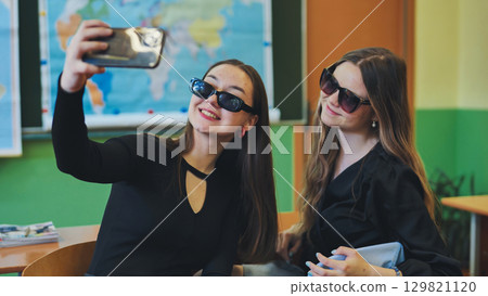 Two happy young women students in sunglasses taking a selfie with a smartphone in a classroom Two happy young women students in sunglasses taking a selfie with a smartphone in a classroom 129821120