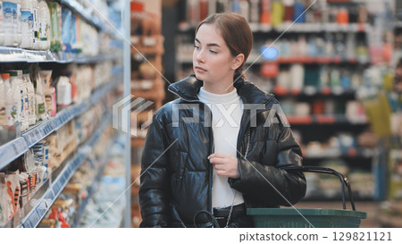 Female shopper selecting dairy products, carrying grocery basket in supermarket aisle Female shopper selecting dairy products, carrying grocery basket in supermarket aisle 129821121