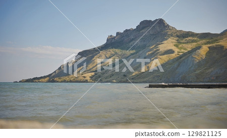 Breathtaking landscape showcasing crimean mountains meeting the black sea, featuring waves gently lapping against the shore on a clear, sunny day. 129821125