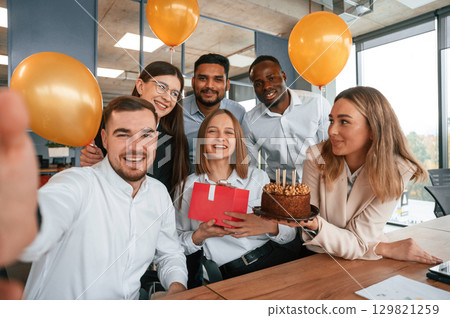 Selfie of happy woman with gift. Employee having a birthday in the office, group of workers 129821259