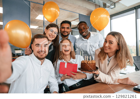 Selfie of happy woman with gift. Employee having a birthday in the office, group of workers 129821261