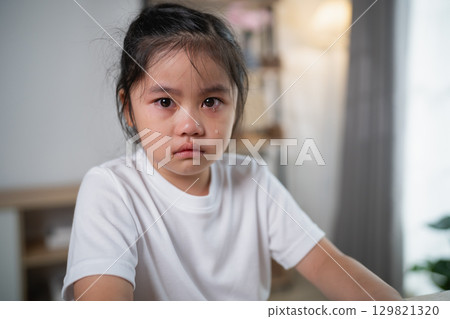 Sad young girl with tearful eyes looking into the camera while sitting indoors, expressing emotions of distress and unhappiness in a cozy room setting Sad young girl with tearful eyes looking into the camera while sitting indoors, expressing emotions of distress and unhappiness in a cozy room setting 129821320
