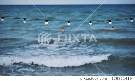 String of lights illuminating the beach of Crimea with tourists swimming in the sea String of lights illuminating the beach of Crimea with tourists swimming in the sea 129821419