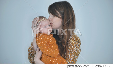 Young mother kissing her baby girl on the forehead, showing love and care in a heartwarming family moment 129821425