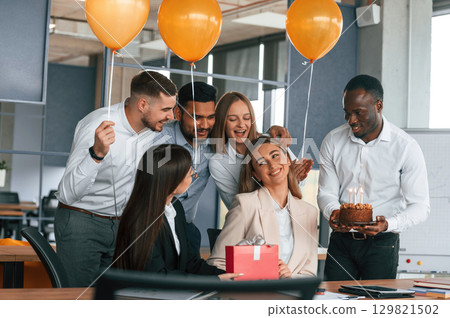 Celebration with cake, balloons and gift box. Employee having a birthday in the office, group of workers 129821502