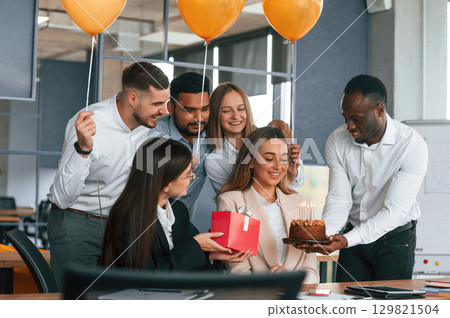 Celebration with cake, balloons and gift box. Employee having a birthday in the office, group of workers 129821504