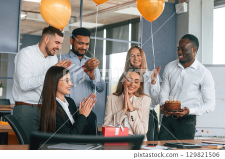 Celebration with cake, balloons and gift box. Employee having a birthday in the office, group of workers Celebration with cake, balloons and gift box. Employee having a birthday in the office, group of workers 129821506