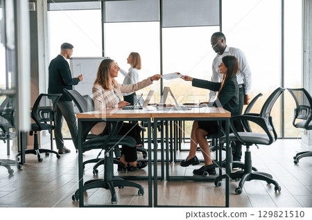 Giving the documents. Group of office workers are together indoors Giving the documents. Group of office workers are together indoors 129821510