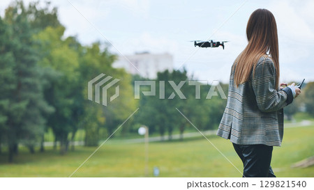 Businesswoman skillfully pilots a drone in a lush city park, showcasing the integration of technology and leisure 129821540