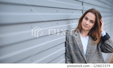 Confident businesswoman posing against a gray metal wall, touching her hair with a serene expression 129821574