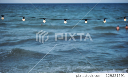 String of lights illuminating Crimean beach with tourists swimming in the Black Sea String of lights illuminating Crimean beach with tourists swimming in the Black Sea 129821591