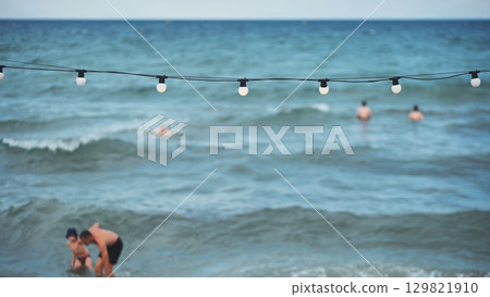 String of lights illuminating Crimean beach with tourists enjoying summer vacation String of lights illuminating Crimean beach with tourists enjoying summer vacation 129821910