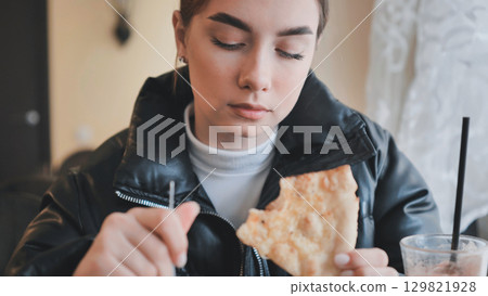 Young woman biting pizza slice, smiling while dining casually with friends Young woman biting pizza slice, smiling while dining casually with friends 129821928