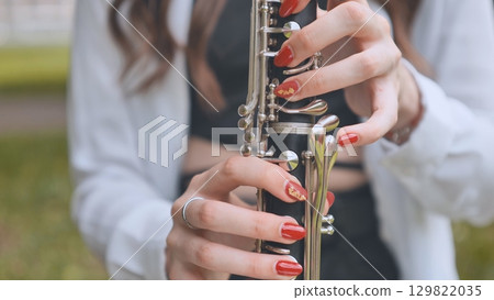 Musician's hands gripping clarinet keys while performing outdoors, revealing detailed woodwind craftsmanship and professional playing technique 129822035