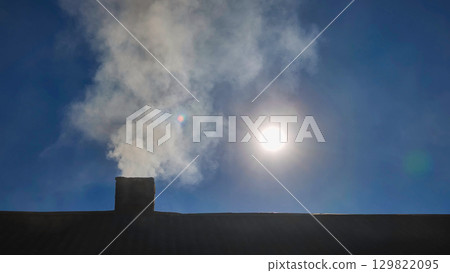 Chimney smoke curling skyward, silhouetted against deep twilight blue, radiating cozy winter evening tranquility Chimney smoke curling skyward, silhouetted against deep twilight blue, radiating cozy winter evening tranquility 129822095