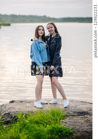 Two young women hugging each other, standing on a rock by the lake, enjoying their friendship Two young women hugging each other, standing on a rock by the lake, enjoying their friendship 129822231
