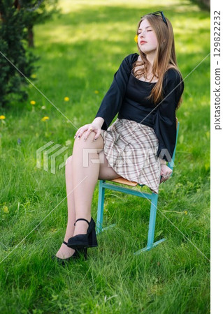 Young student relaxing on a chair in a sunny, grassy outdoor space during a school day Young student relaxing on a chair in a sunny, grassy outdoor space during a school day 129822232