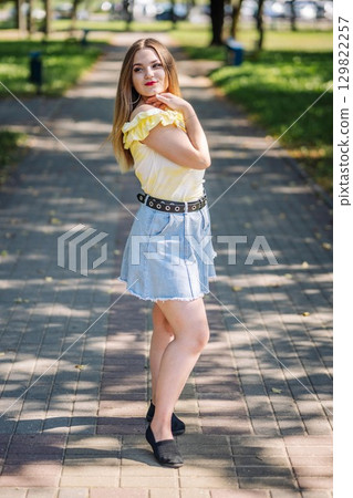 Young woman enjoying sunny park day, wearing yellow t shirt and denim skirt Young woman enjoying sunny park day, wearing yellow t shirt and denim skirt 129822257