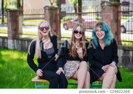 Three happy students in shades share a laugh while hanging out on a bench in the schoolyard during a break Three happy students in shades share a laugh while hanging out on a bench in the schoolyard during a break 129822268