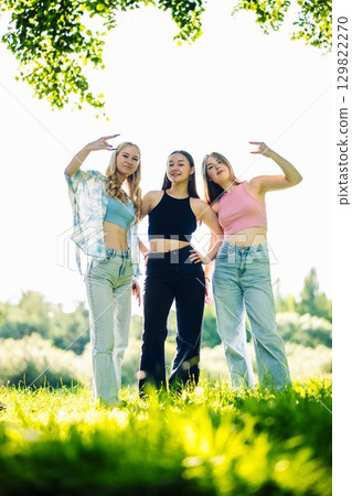 Young women gesturing rock and roll on grassy meadow during sunny summer afternoon Young women gesturing rock and roll on grassy meadow during sunny summer afternoon 129822270