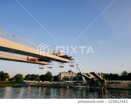 Construction workers raising prefabricated bridge segments using large cranes near Vistula River in Krakow, Poland, highlighting urban infrastructure progress and engineering complexity. Construction Construction workers raising prefabricated bridge segments using large cranes near Vistula River in Krakow, Poland, highlighting urban infrastructure progress and engineering complexity. Construction 129822481