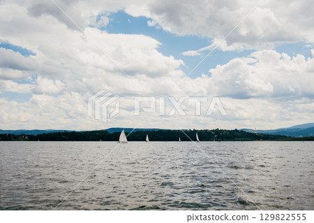 Sailboats gliding across tranquil waters of lake, enjoying beautiful day under cloudy sky, with majestic mountains rising in background, create picturesque scene. Sailboats, lake, mountainous, sky 129822555